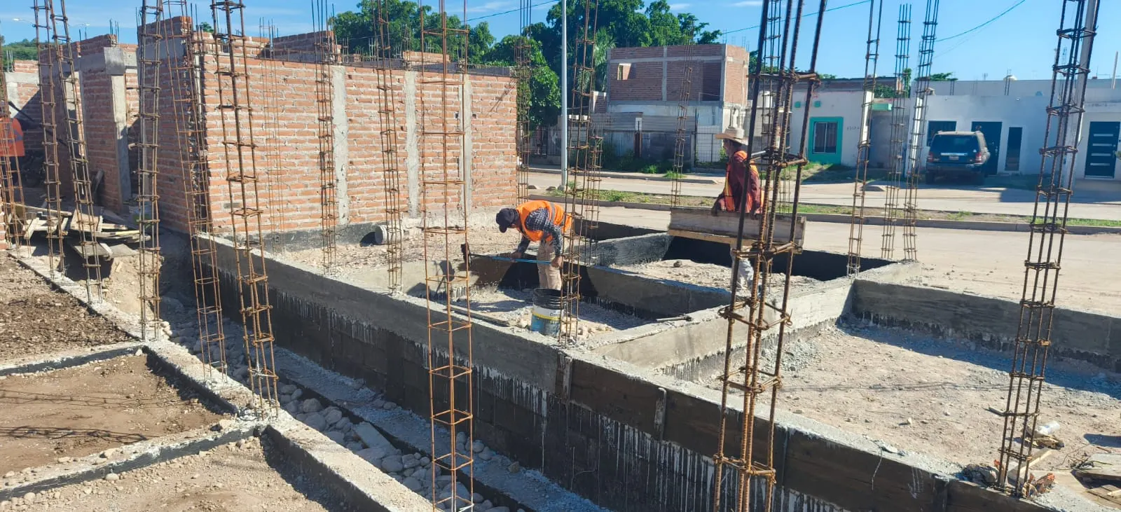 Obreros revisando una cimentación con varillas y muros de ladrillo